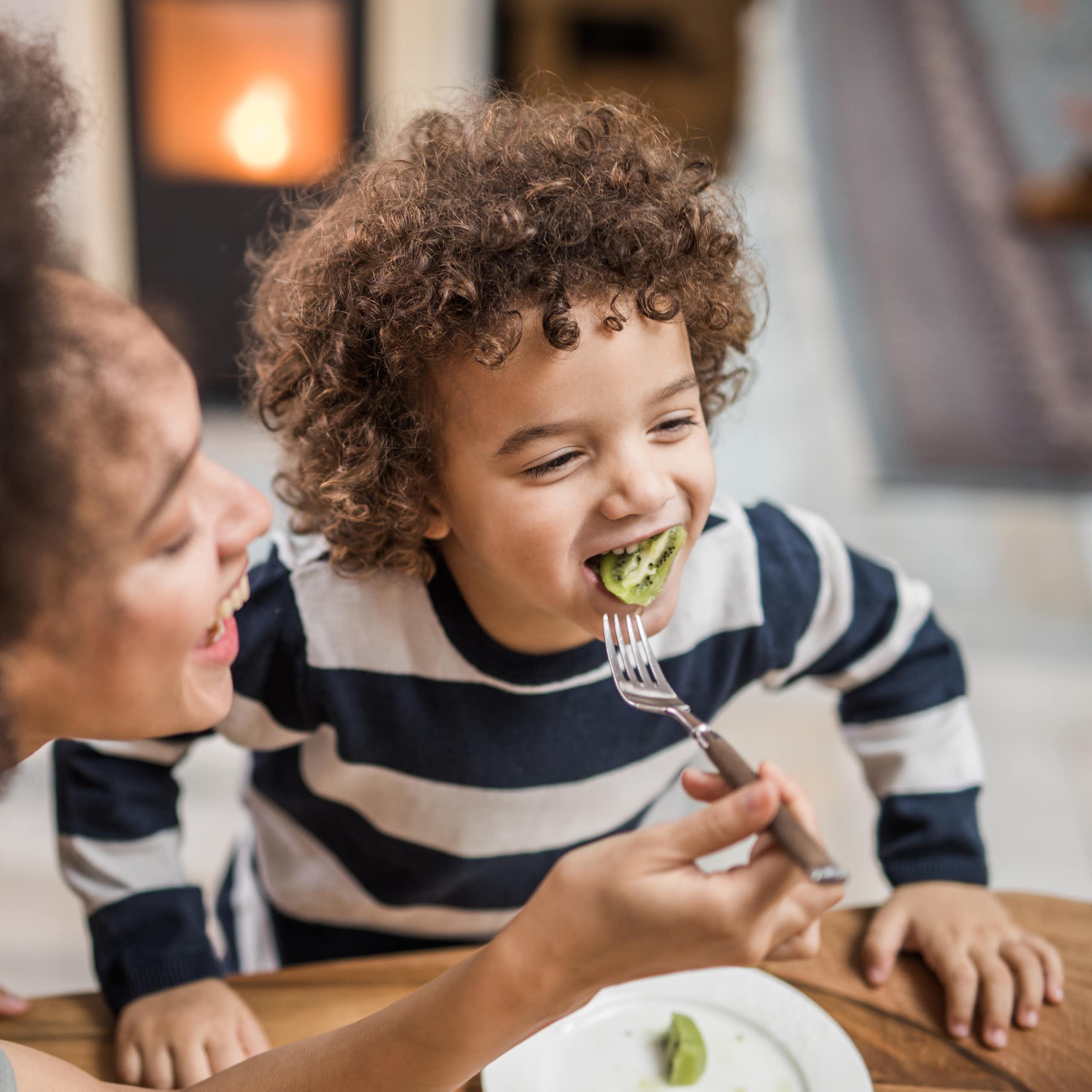 woman holding fork with kiwi in child's mouth