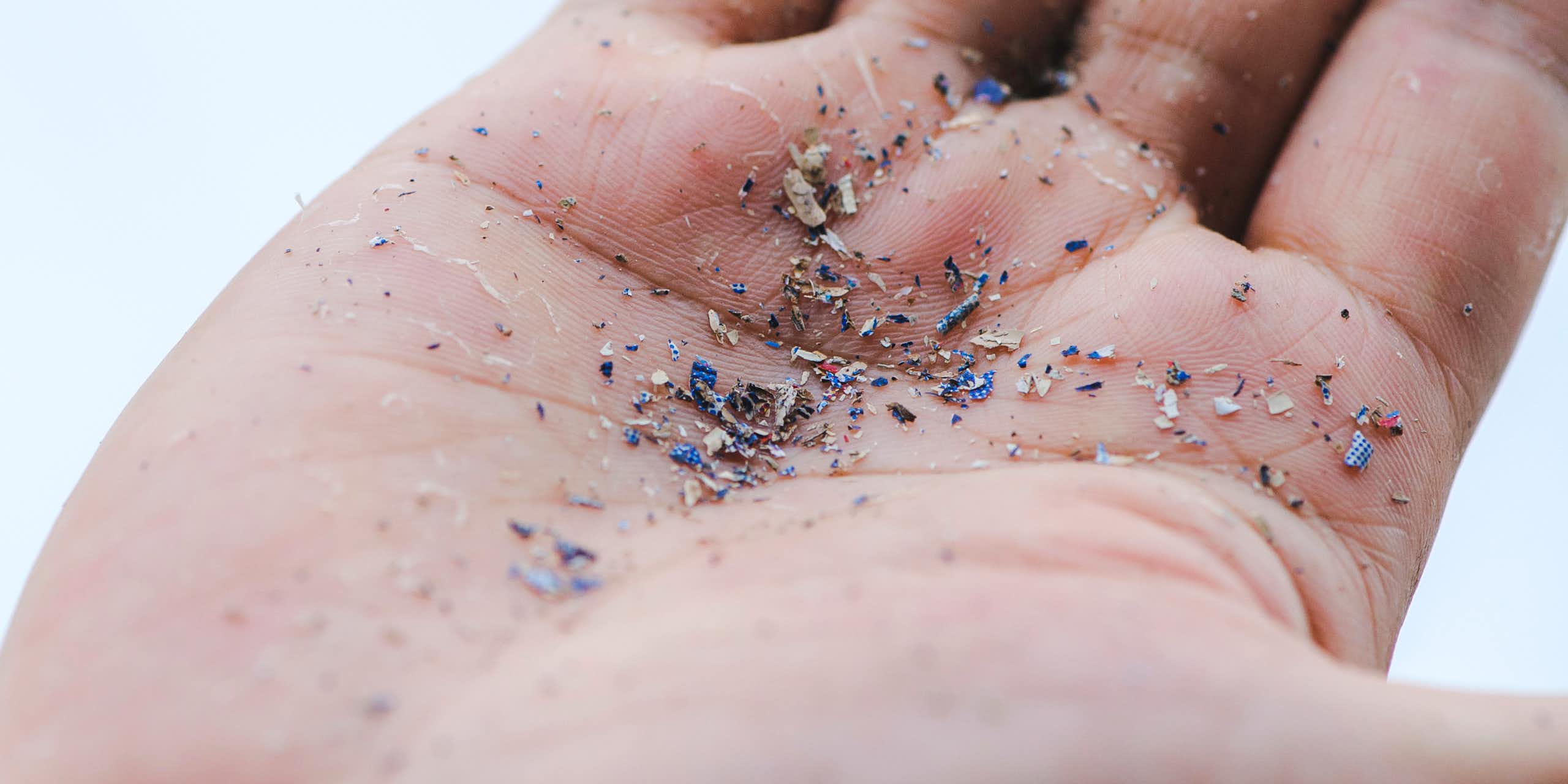 Uma imagem em close da mão de uma pessoa. Em sua palma, ela segura fragmentos de microplásticos