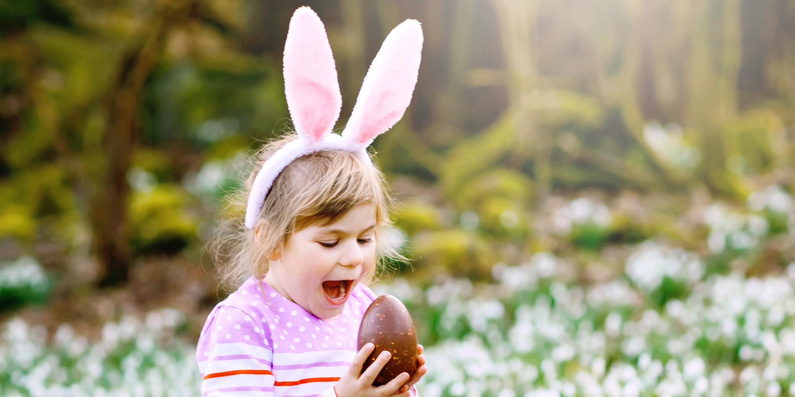 Little girl in bunny ears about to bite into an Easter egg